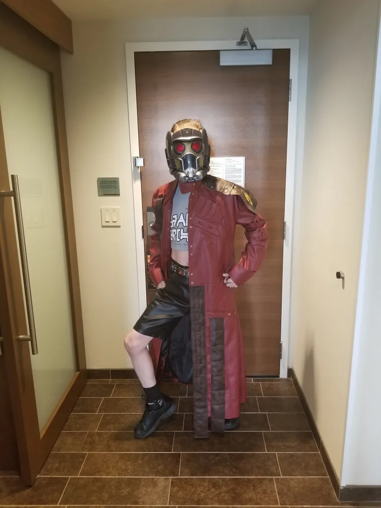 A person in a Star-Lord costume from Guardians of the Galaxy stands in a hotel hallway, posing with hands on hips. The…