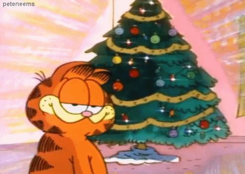 Garfield, the orange tabby cat, stands in front of a decorated Christmas tree with a visibly unimpressed, bored expression…