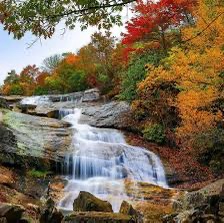 A scenic autumn waterfall surrounded by vibrant red, orange, and yellow foliage under a clear sky. Overlaid text reads 'i'm…