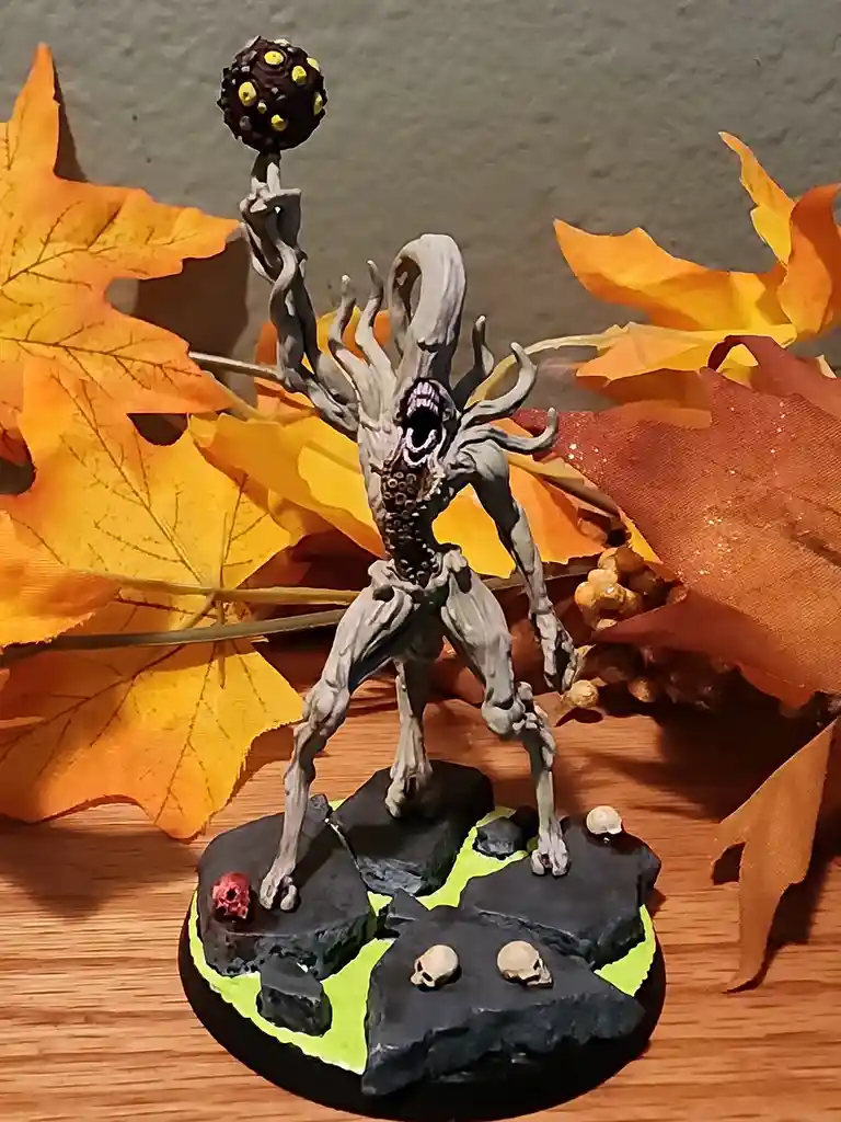 A painted miniature of a grotesque, tree-like monster with a gaping mouth and multiple limbs, holding a spherical object…