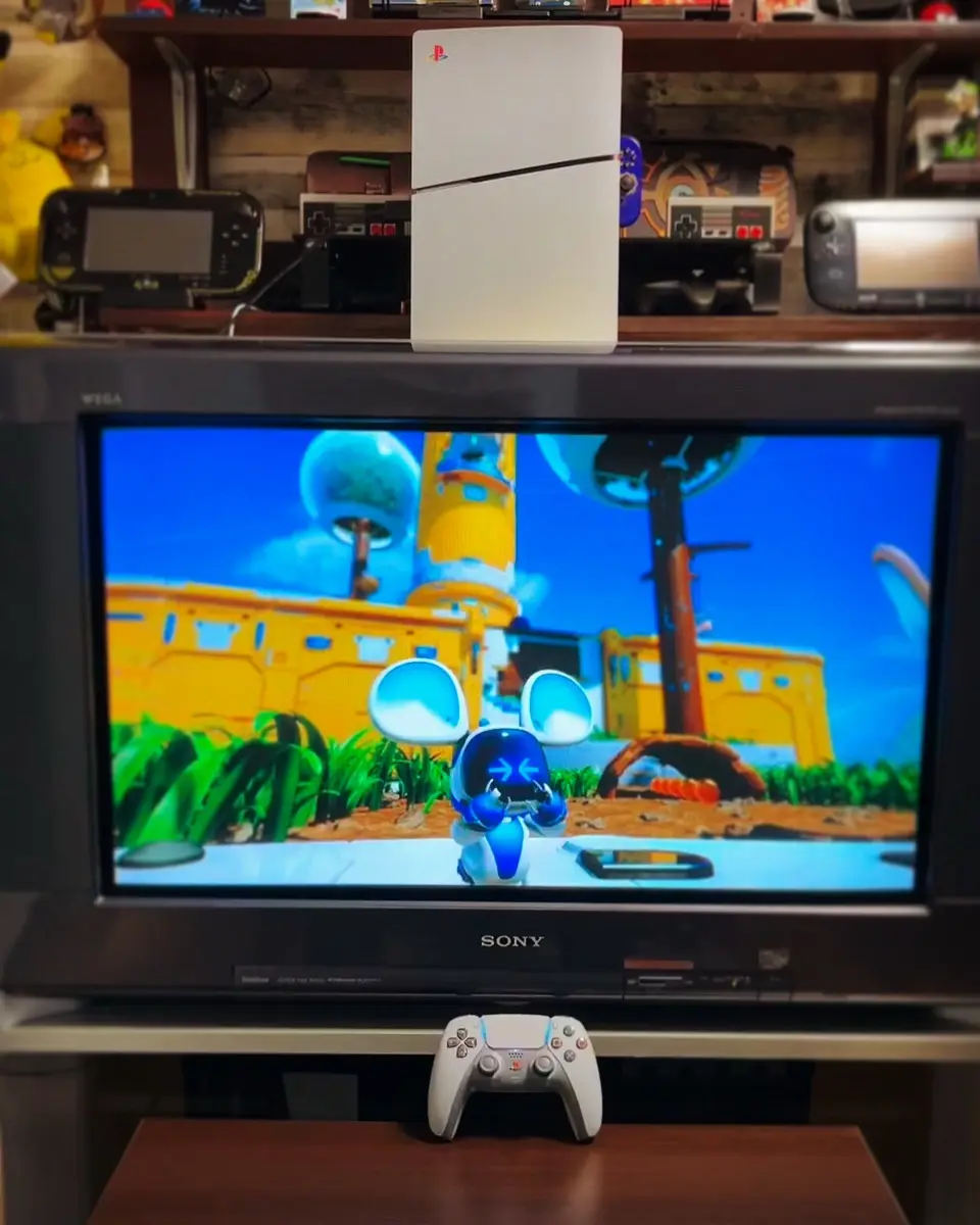 A white PlayStation 5 console sits vertically on top of a CRT television, which displays a scene from the game…
