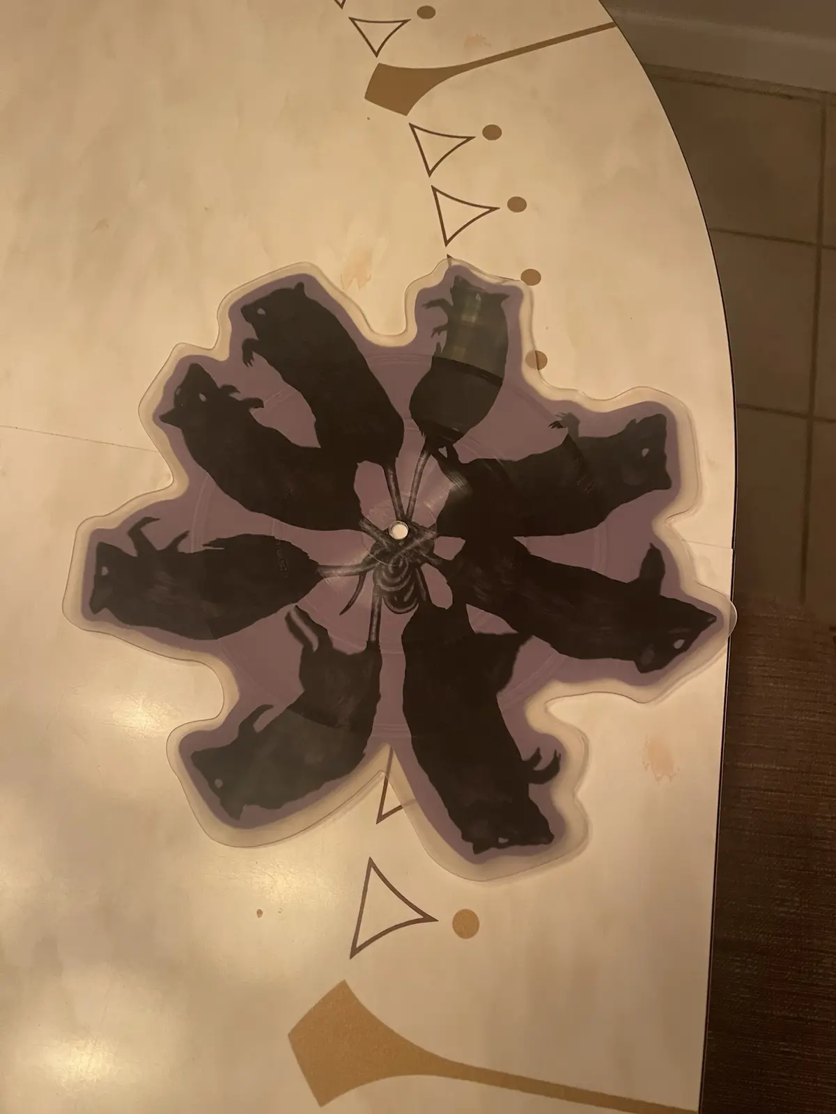 A close-up photo shows a decorative tabletop with a large, flower-shaped decal. The decal features eight black silhouettes…