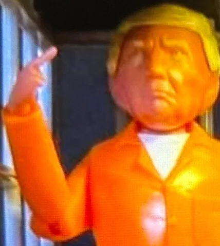 A blurry, low-resolution image shows a plastic action figure resembling Donald Trump, wearing an orange jumpsuit and a…