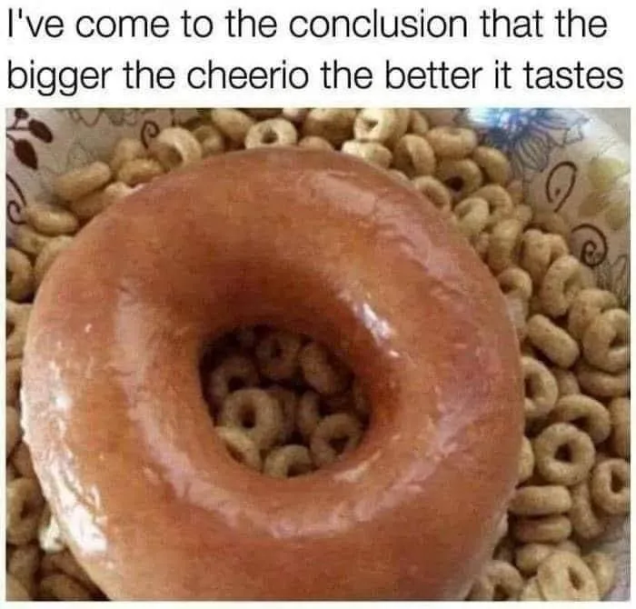 A close-up photo shows a glazed donut placed in the center of a bowl filled with Cheerios cereal. The donut's hole is filled…