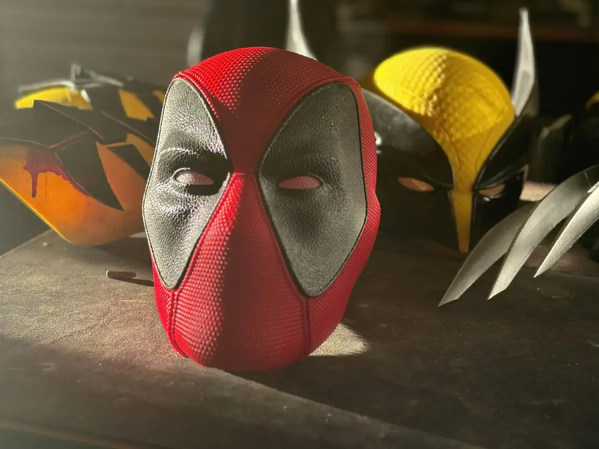 A red and black Deadpool mask sits prominently on a dark surface, surrounded by other superhero masks including a yellow and…
