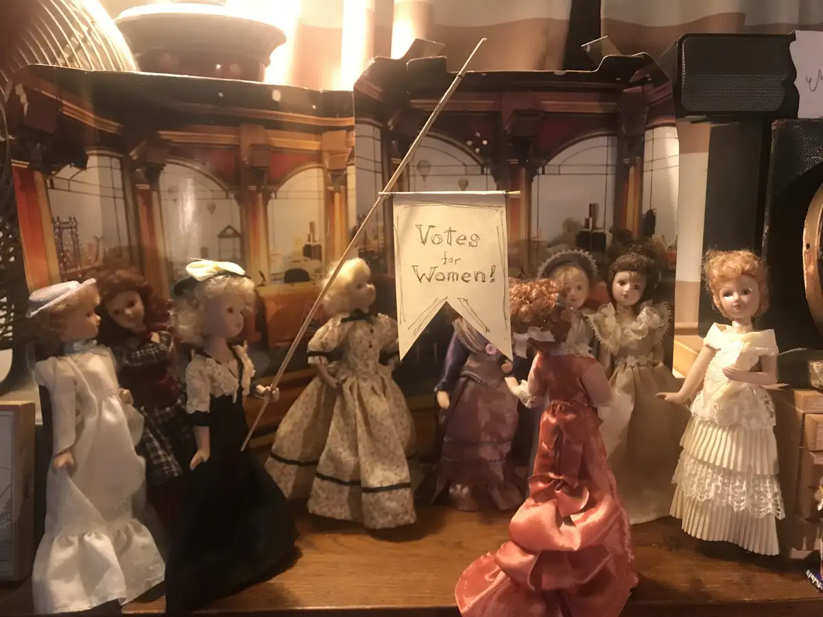 A group of vintage dolls dressed in historical women's clothing are arranged on a wooden surface, one holding a handmade…