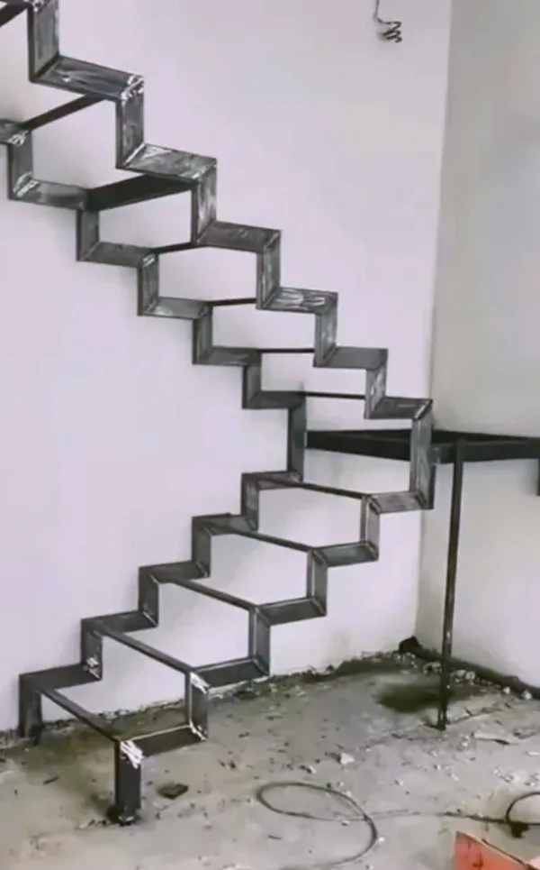 A metal staircase with a zigzag pattern is mounted on a white wall, appearing to float without visible support. The floor…