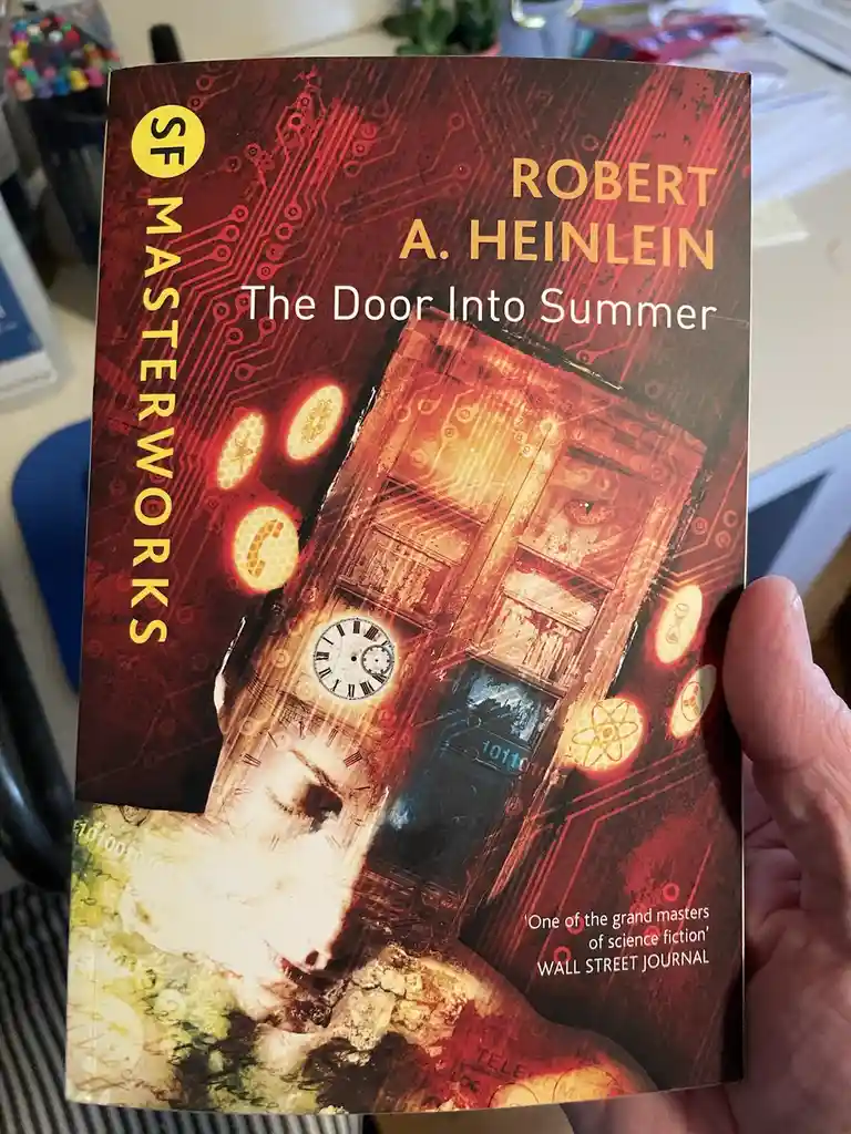 A hand holds a book titled 'The Door Into Summer' by Robert A. Heinlein, part of the 'SF MASTERWORKS' series. The cover art…