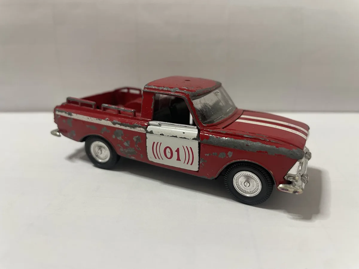 A weathered red toy pickup truck with peeling paint and white racing stripes is shown from a side angle. The driver's side…
