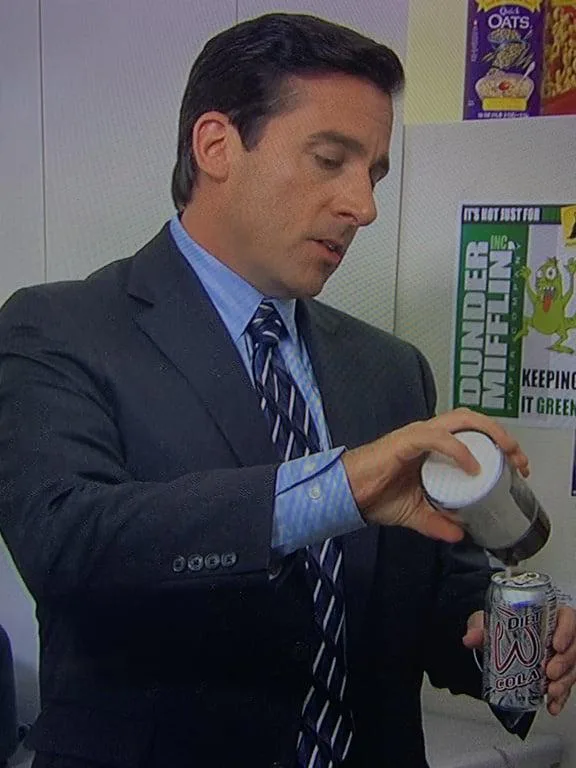 A man in a suit and tie pours a white substance from a container into a can of Diet W Cola. Behind him, a poster for 'Dunder…