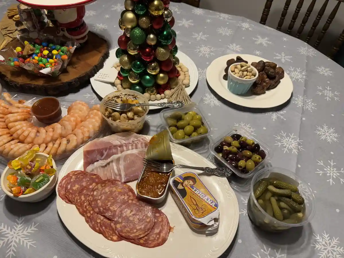 A festive holiday table is laden with an assortment of appetizers including shrimp, salami, ham, olives, pickles…