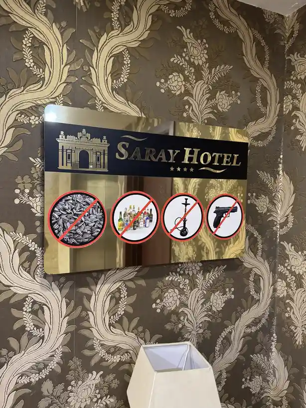 A sign for Saray Hotel displays four prohibitions: sunflower seeds, alcohol, hookah, and handguns, all marked with red…