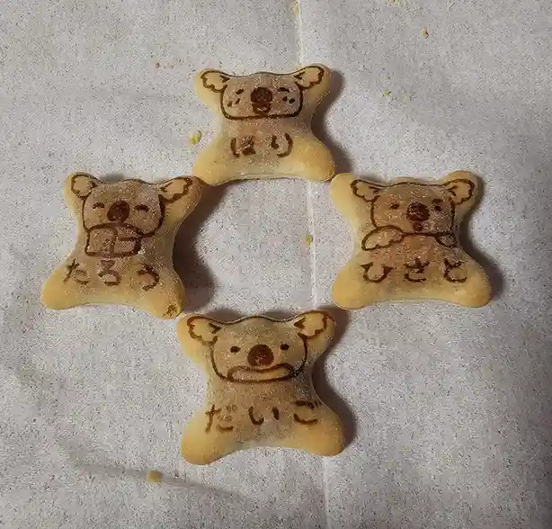 Four bear-shaped cookies arranged in a diamond pattern on a white surface, each with a simple face drawn in brown and…