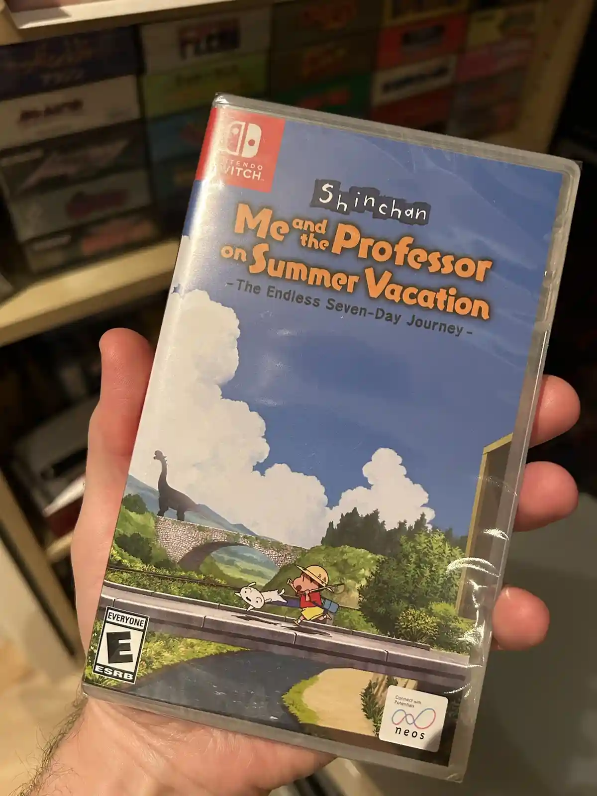 A hand holds a sealed Nintendo Switch game case for 'Shinchan Me and the Professor on Summer Vacation - The Endless…
