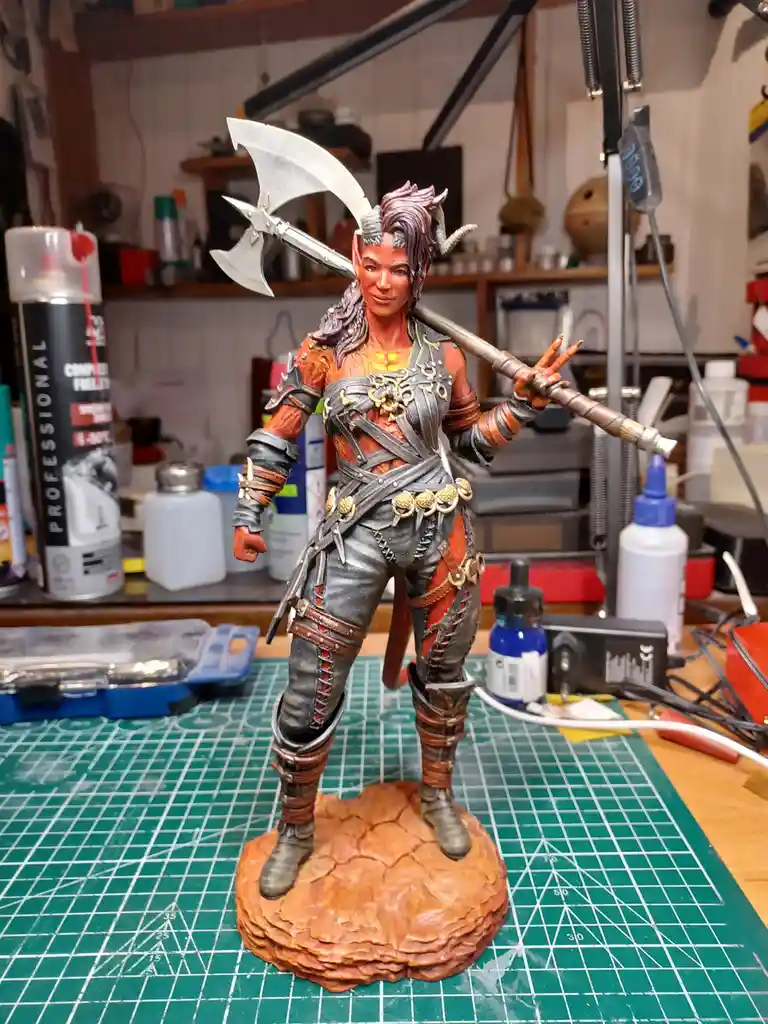 A highly detailed, painted fantasy figurine of a female warrior with horns, wielding a large axe over her shoulder, stands…