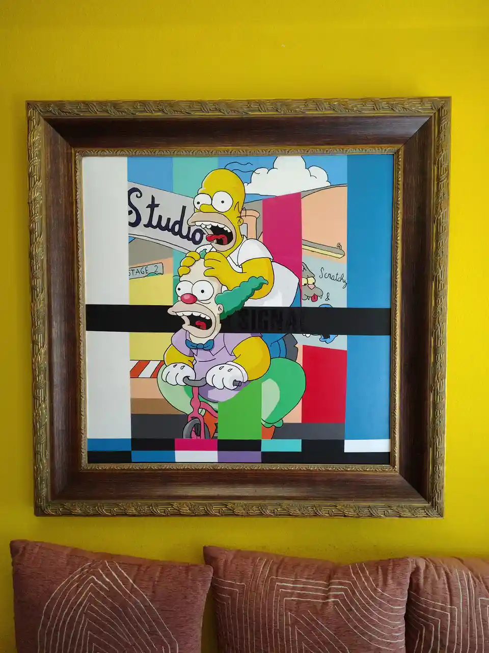 A framed painting of Homer Simpson riding a bicycle while holding a clown, with a black bar across the middle displaying the…
