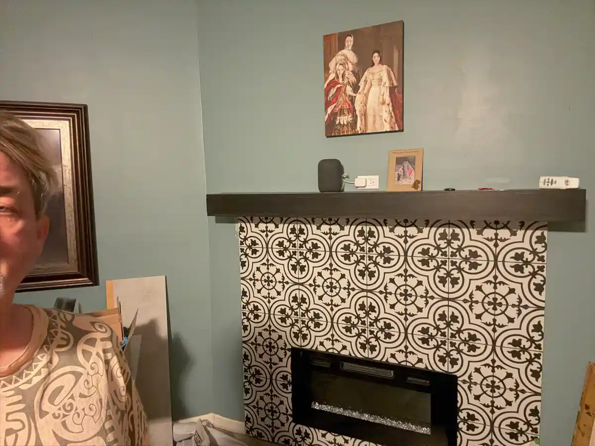 A person partially visible on the left stands in front of a fireplace with black-and-white patterned tiles. Above the mantel…