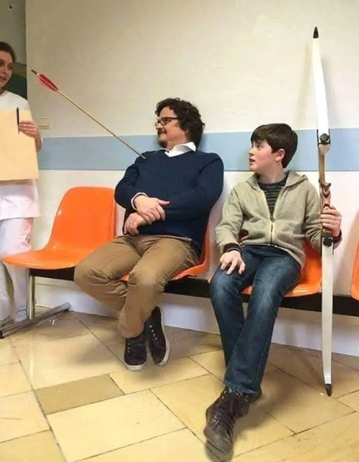 In a hospital waiting room, a man with glasses sits calmly on an orange bench with an arrow stuck in his head, while a boy…