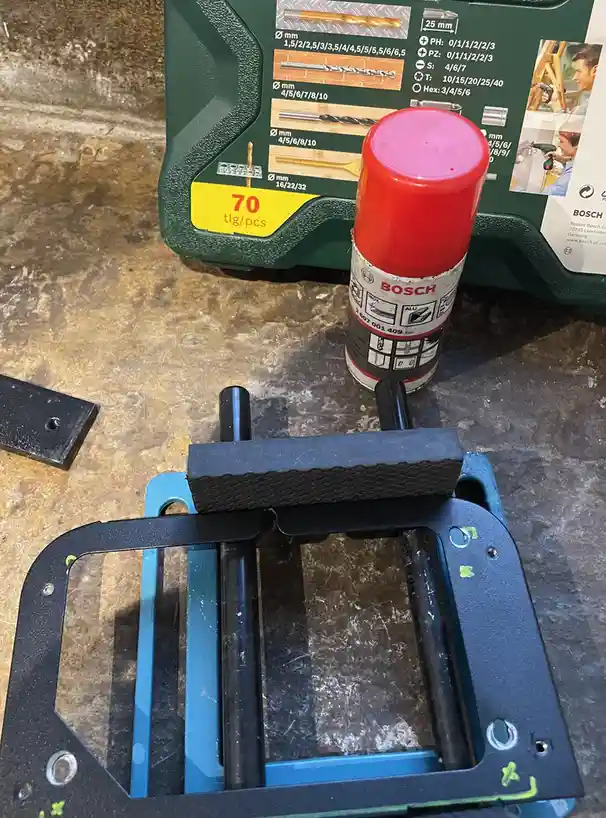 A close-up photo shows a Bosch spray can, a green Bosch drill bit set case, and a metal bracket with a black foam pad…