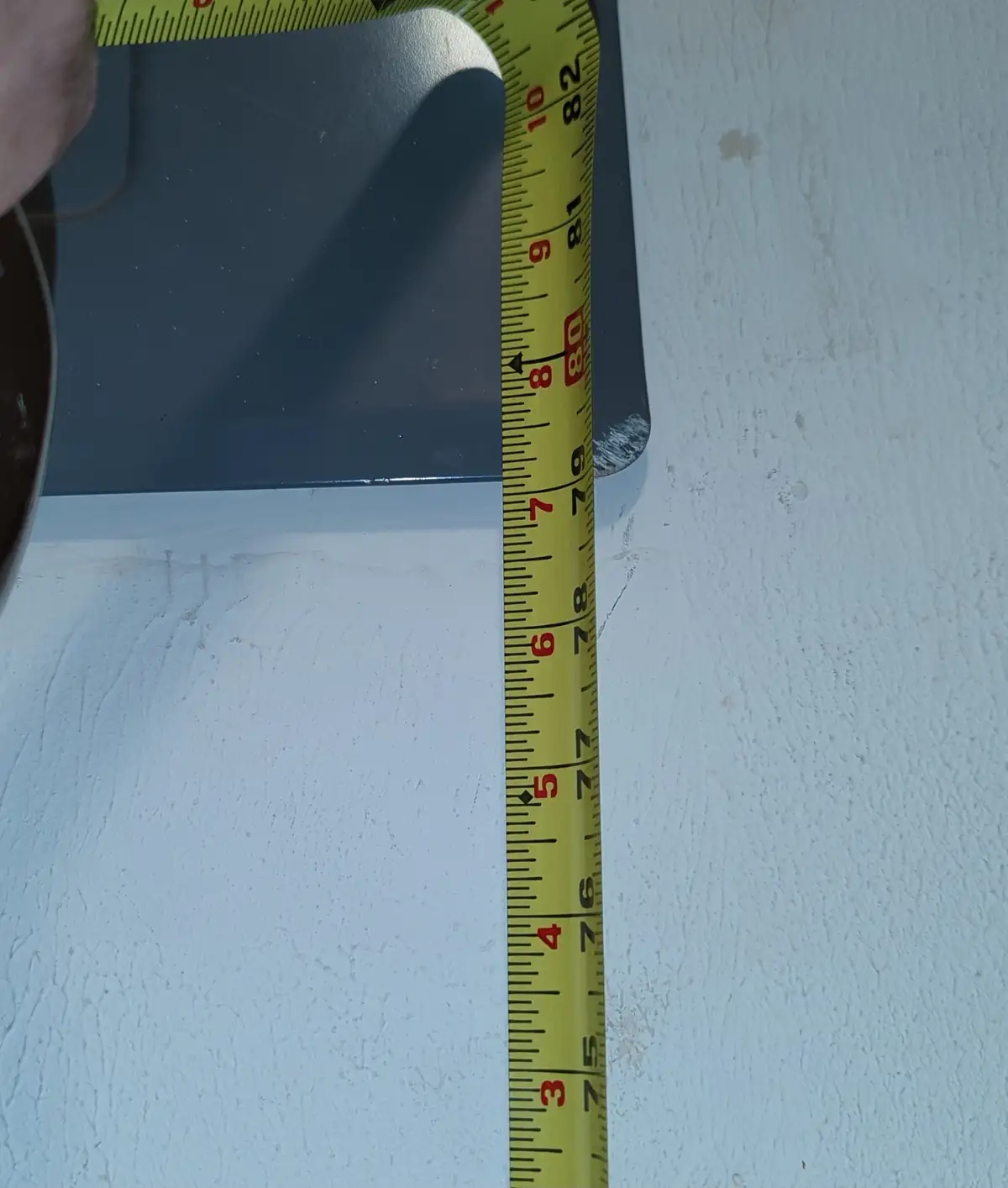 A close-up photo shows a yellow measuring tape being held against a dark gray, curved object, likely a piece of furniture or…