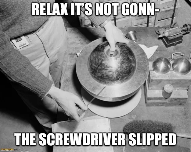 A black-and-white photo shows a person in a sweater and pants using a screwdriver on a large, round, metallic object. The…