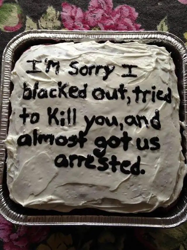 A rectangular cake with white frosting in a foil pan has black icing text that reads 'I'M Sorry I blacked out, tried to Kill…