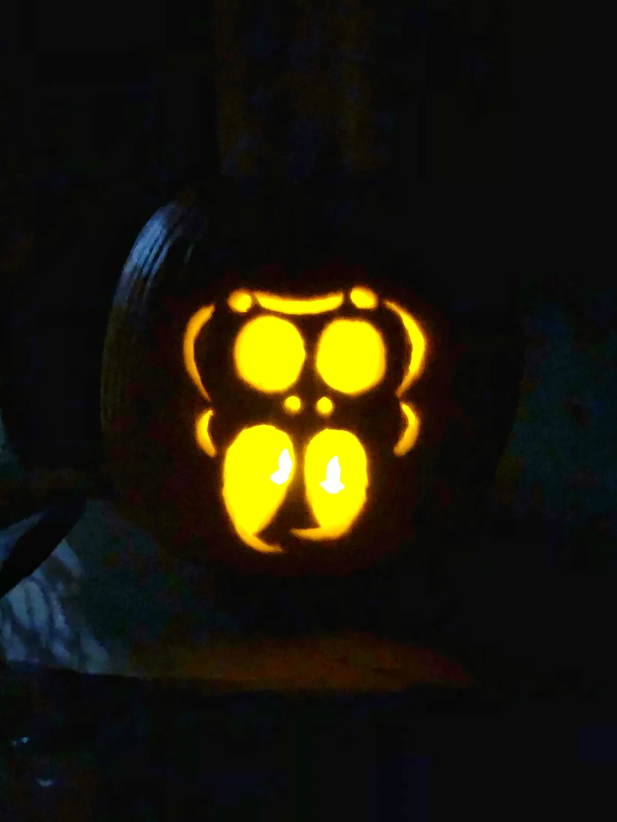 A carved pumpkin with glowing eyes and mouth is lit from within in a dark room, its face designed to resemble a revolver…