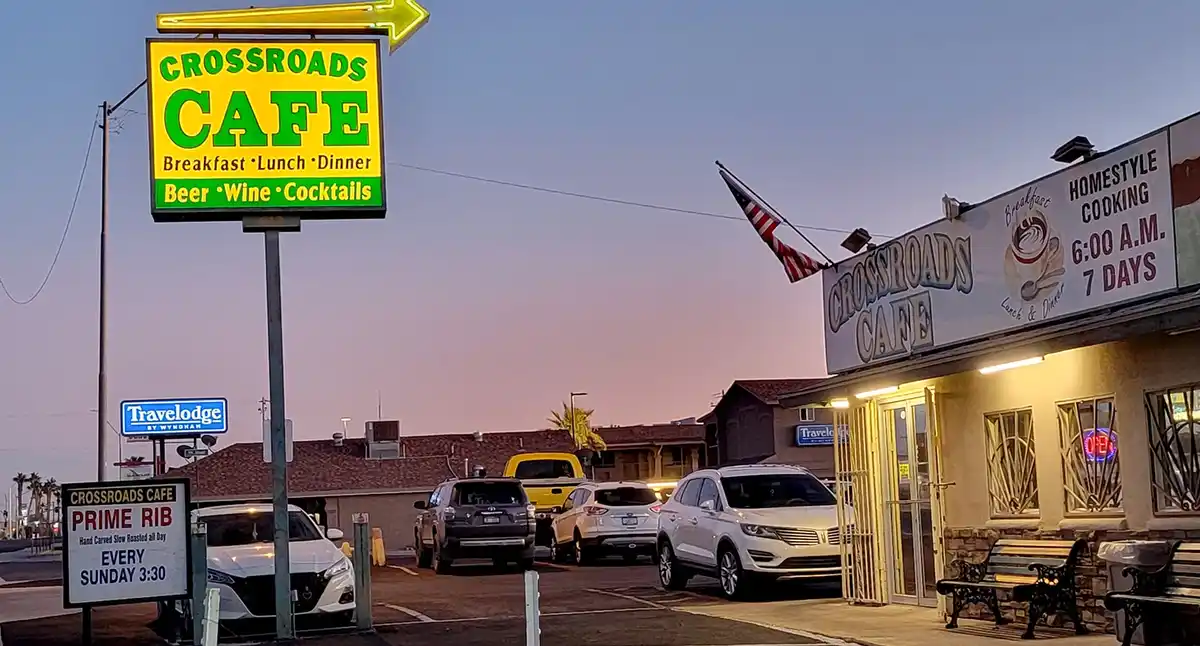 An exterior photo of Crossroads Cafe at dusk, showing its large yellow sign advertising breakfast, lunch, dinner, beer…