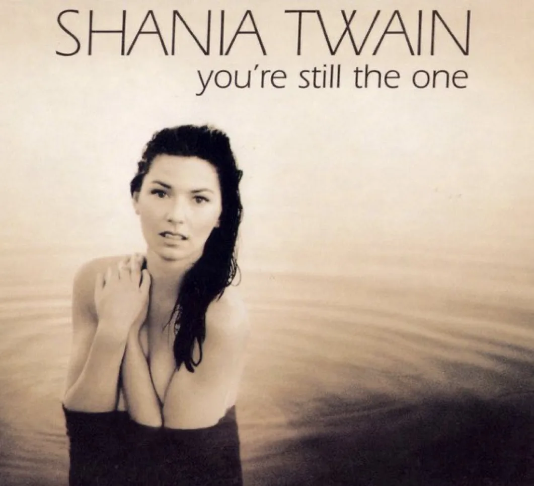 The image is the cover art for Shania Twain's 2002 song 'You're Still the One,' showing her standing waist-deep in water…