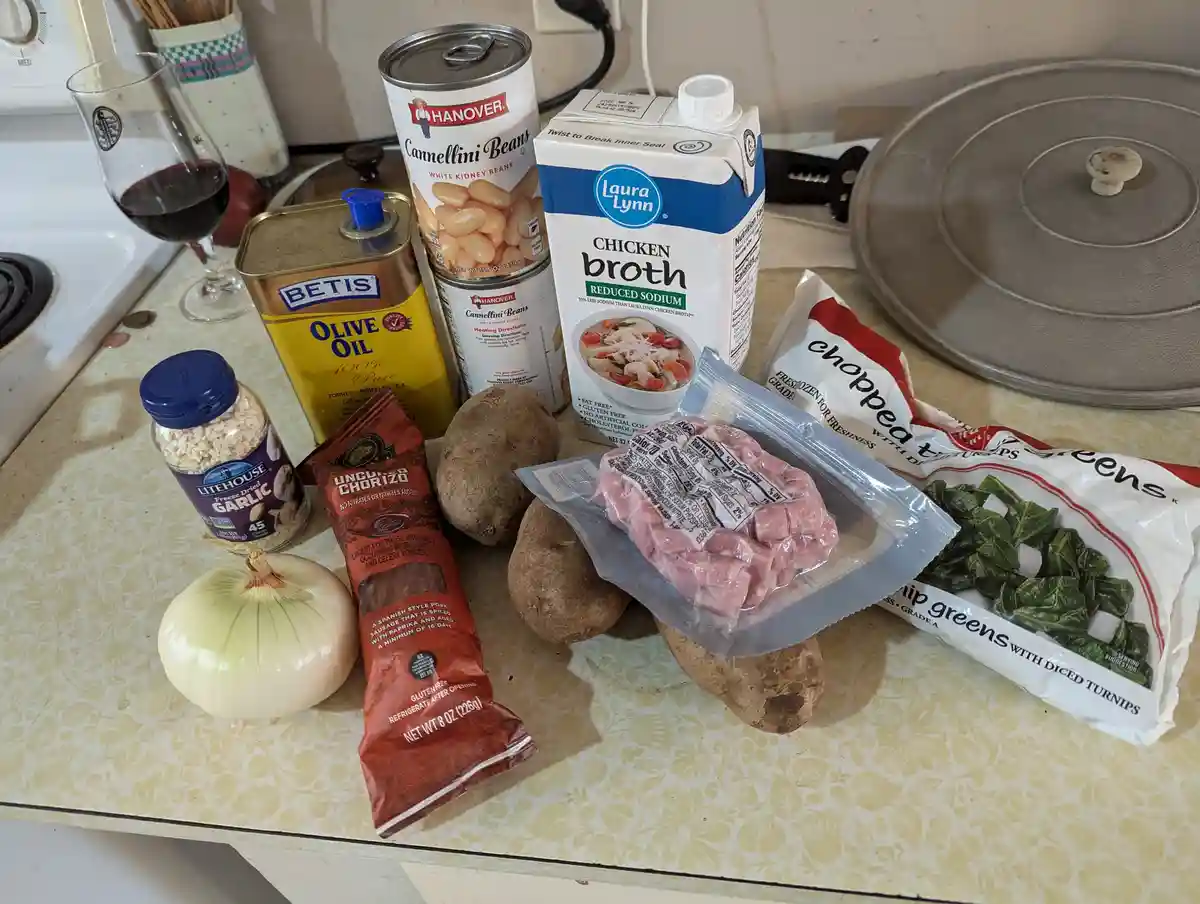 A kitchen counter displays various cooking ingredients including a glass of red wine, olive oil, canned beans, chicken…