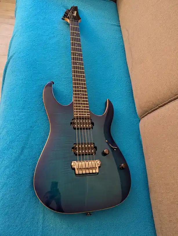 A dark blue electric guitar with a glossy finish and visible wood grain is laid horizontally on a bright blue textured…