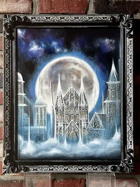 A framed painting depicts a gothic cathedral under a large, glowing moon against a dark, starry sky. The artwork is hung on…