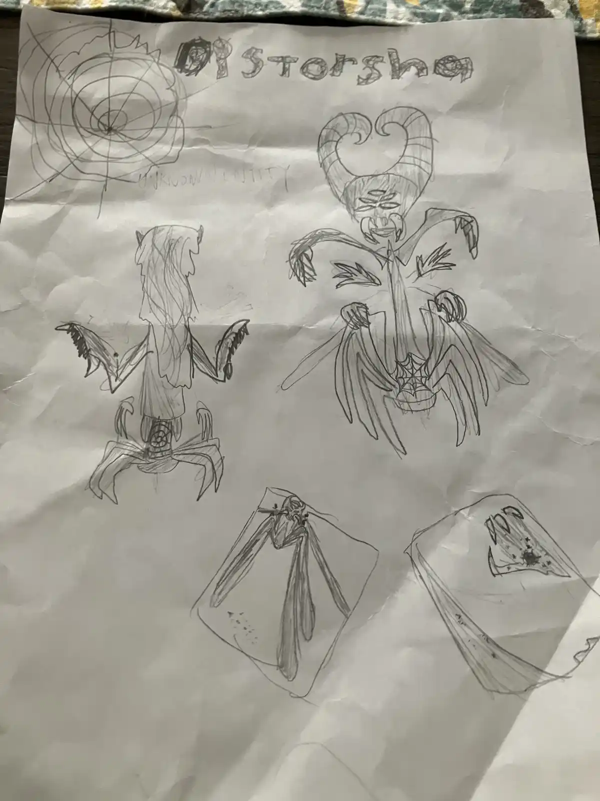 A crumpled piece of paper displays several rough pencil sketches of fantastical, monstrous creatures with wings, horns, and…