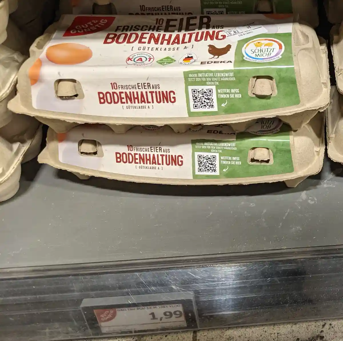 Two stacked egg cartons from EDEKA are shown on a supermarket shelf, labeled '10 FRISCHE EIER AUS BODENHALTUNG [ GÜTEKLASSE…