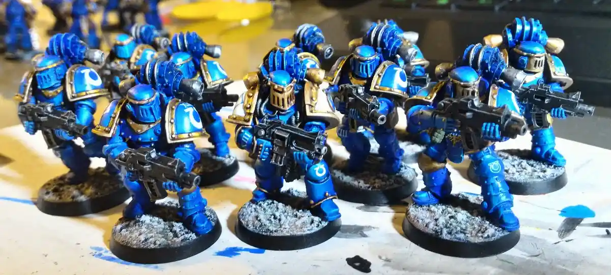 A photo shows a group of painted miniature figurines, resembling Space Marines from Warhammer 40,000, all uniformly coated…