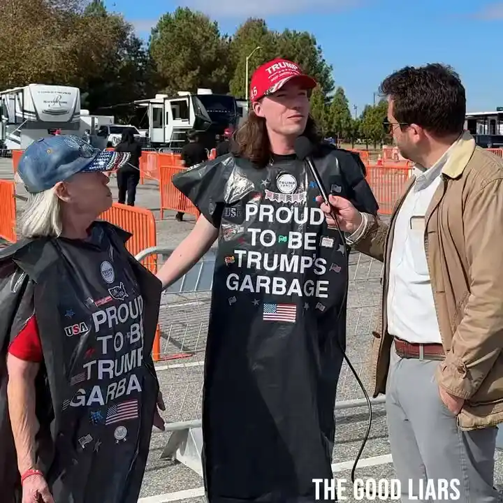 Two people wearing black garbage bag costumes with 'PROUD TO BE TRUMPS GARBAGE' printed on them are being interviewed by a…