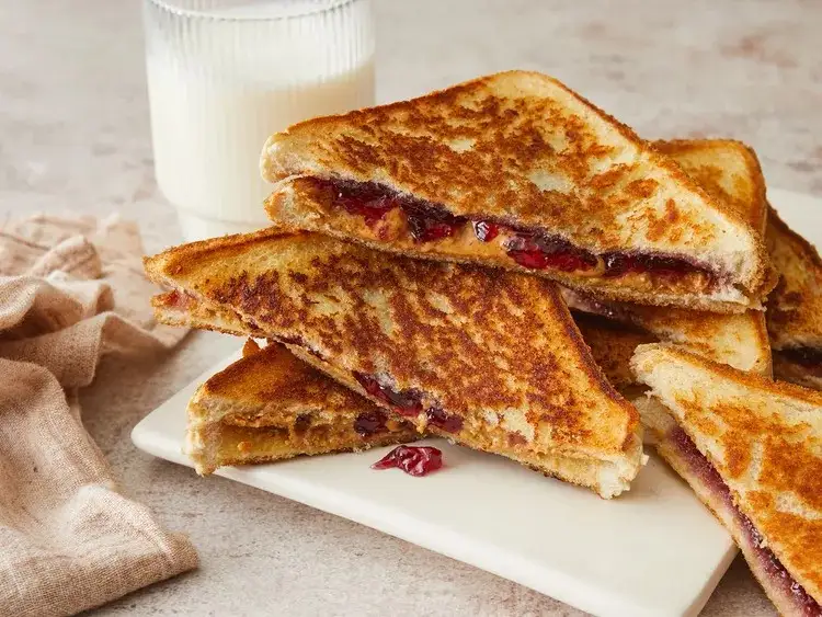 A stack of golden-brown grilled peanut butter and jelly sandwiches cut diagonally, revealing the red jelly and brown peanut…