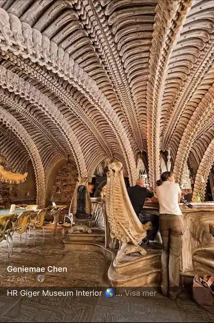 The image shows the interior of a museum with bone-like, biomechanical architecture, featuring arched ceilings and pillars…