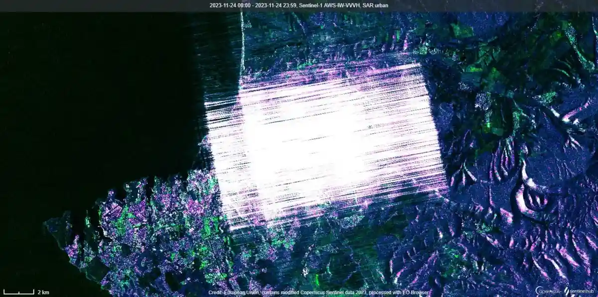 a satellite image from Sentinel-1 shows a city area with a large, bright white rectangular shape dominating the center…