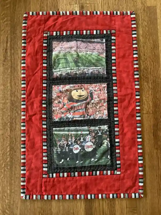 A handmade quilt with a red border and striped trim displays three photos: a football field with marching band formations…