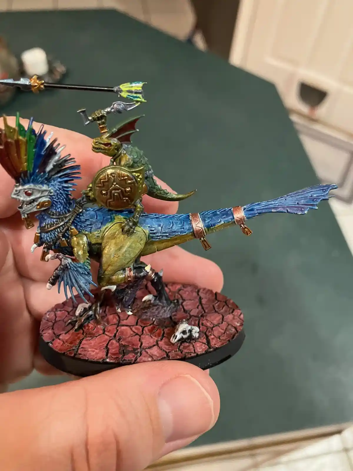 A hand holds a highly detailed, painted miniature of a dragon rider, featuring a blue-feathered, ornate creature with a…