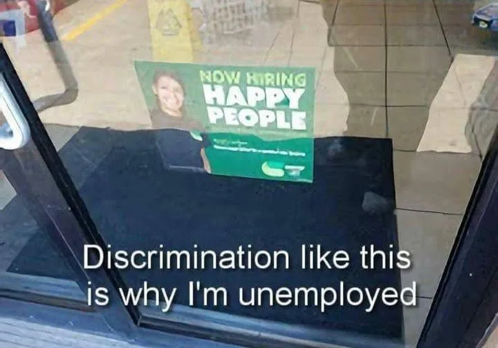 A photo of a glass door with a green 'NOW HIRING HAPPY PEOPLE' sign taped to it, viewed from outside. A black doormat is…