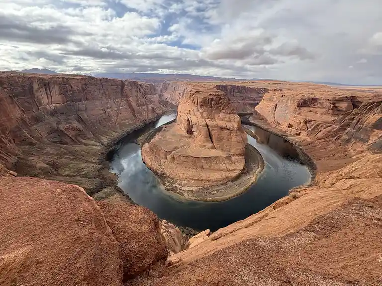 A wide-angle photograph of Horseshoe Bend, Arizona, showing the Colorado River curving sharply around a massive sandstone…