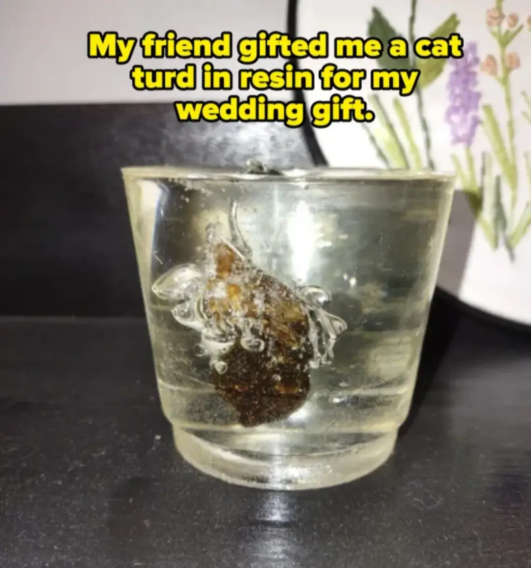 A small, clear glass tumbler sits on a dark surface, containing a brown, irregularly shaped object encased in transparent…
