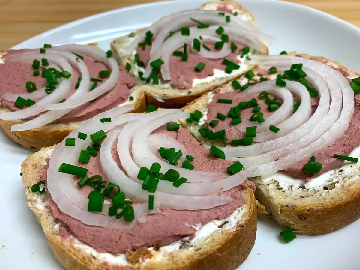 A close-up photo shows four slices of toasted bread on a white plate, each topped with a layer of pink pâté, arranged in a…