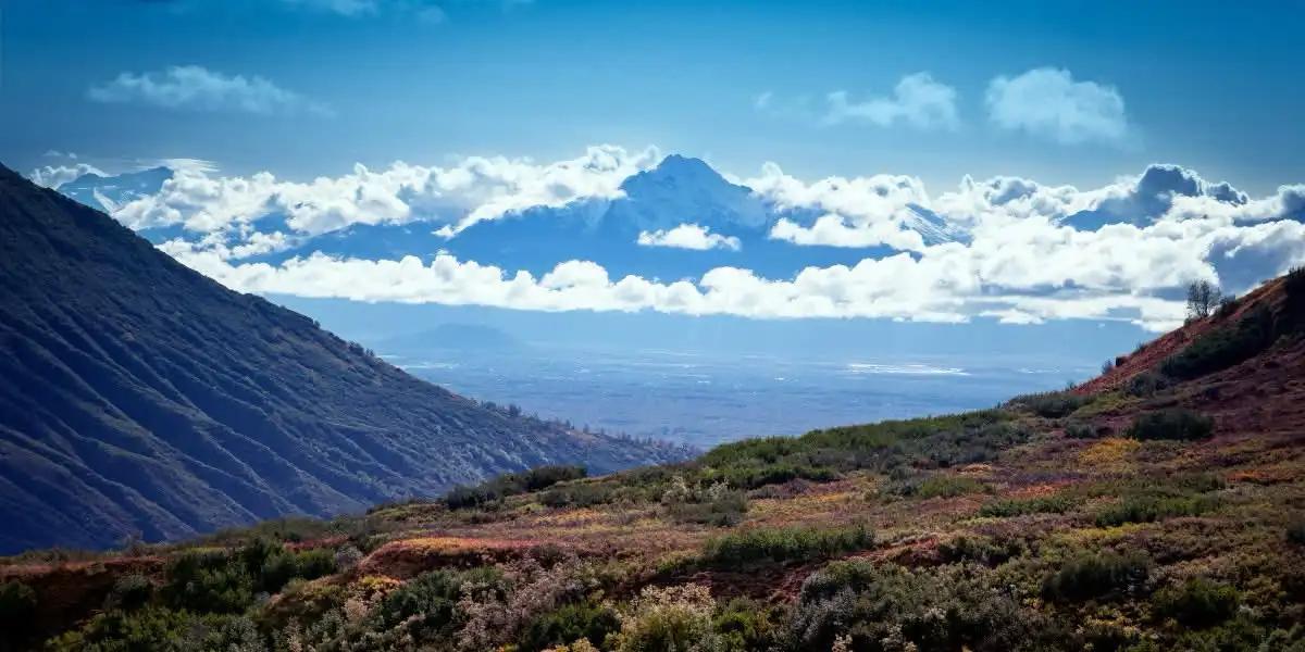 A scenic mountain landscape with a valley below, snow-capped peaks in the distance, and colorful autumn foliage in the…