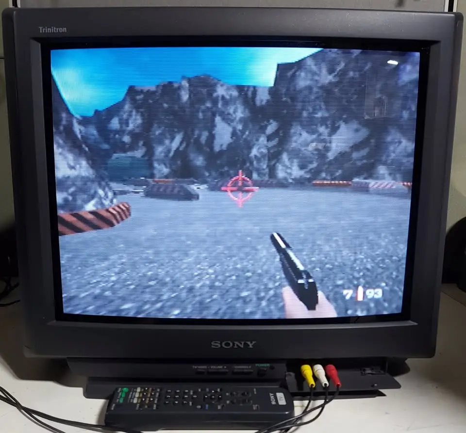 A Sony Trinitron CRT monitor displays a first-person shooter game with a pistol in hand, a red crosshair, and the ammo count…