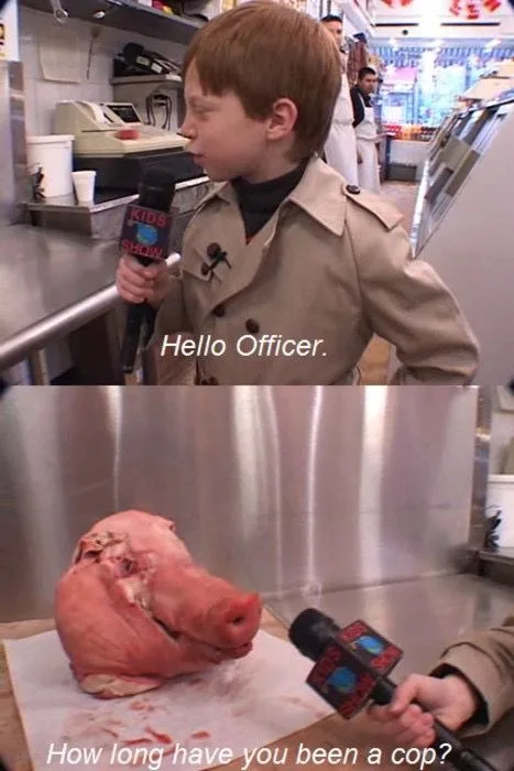 A young boy in a tan trench coat holds a microphone labeled 'KIDS SHOW' and addresses a pig's head on a butcher counter…