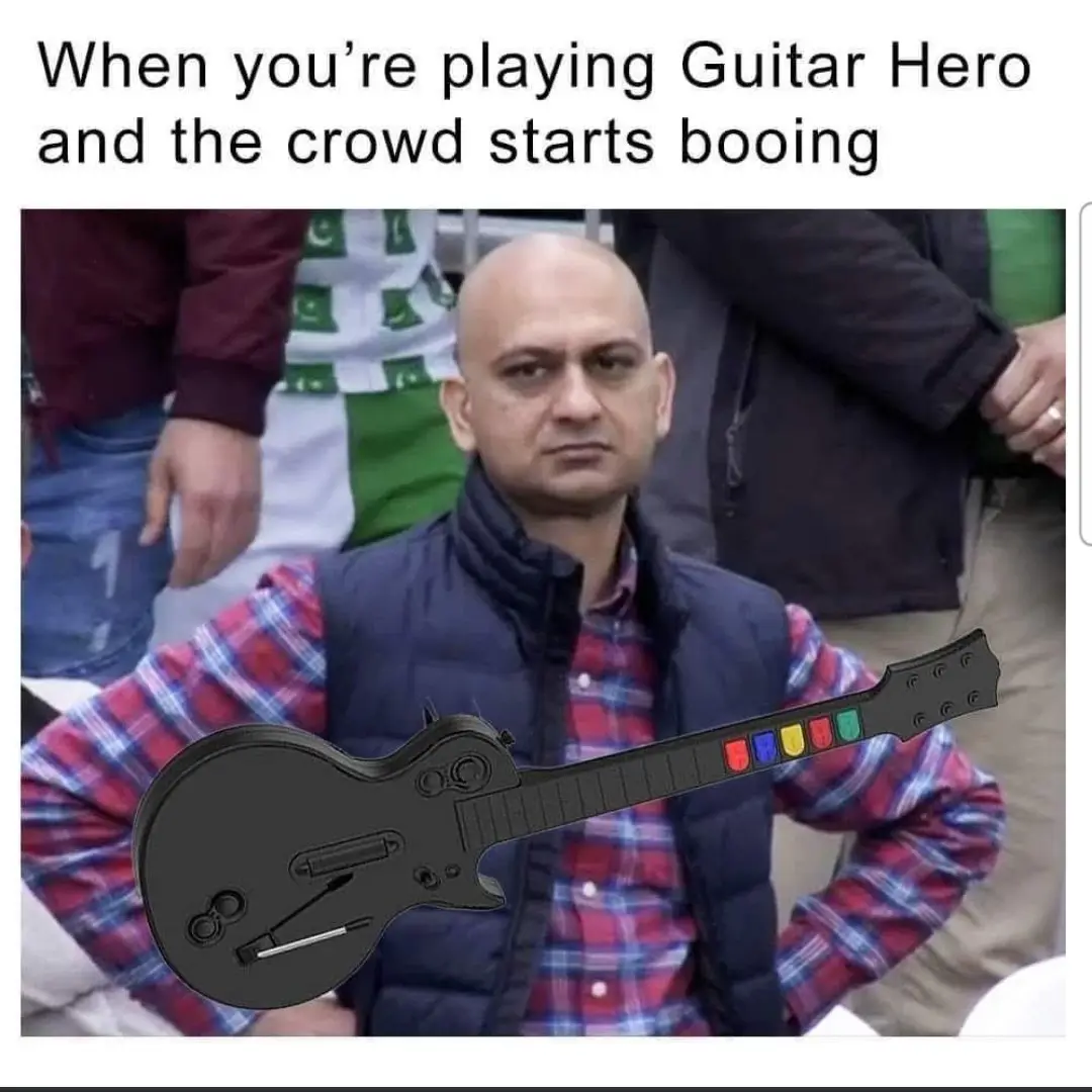 A man in a plaid shirt and vest stares intensely forward while a black Guitar Hero controller is superimposed over his…