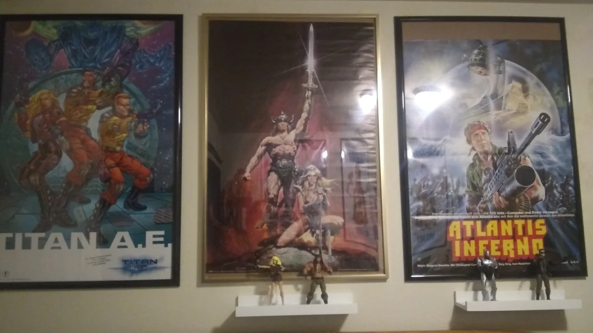 Three framed movie posters hang on a wall: 'Titan A.E.', 'Conan the Barbarian', and 'Atlantis Inferno'. Below each poster…